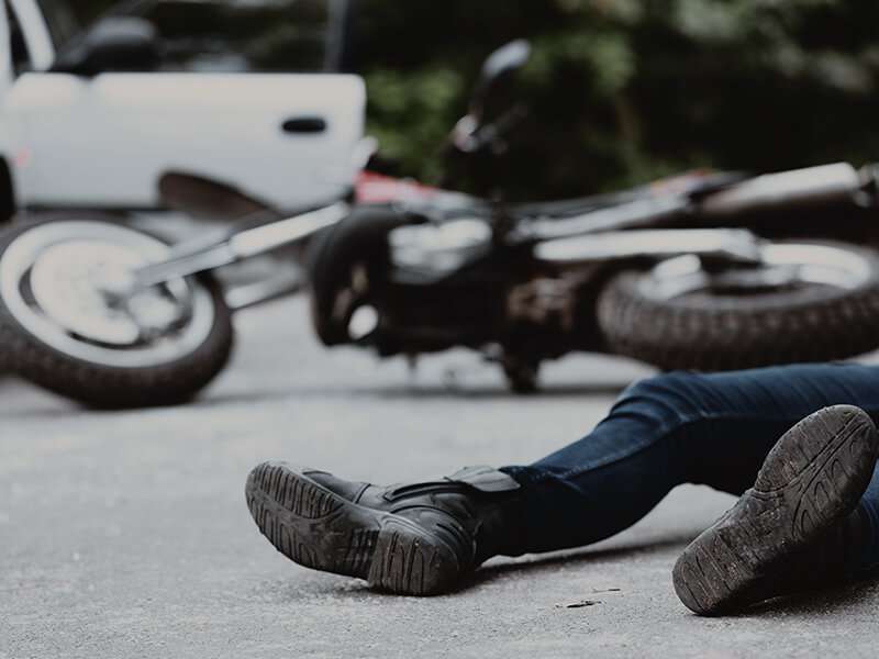 A man laying on the street with a fallen motorcycle in the background